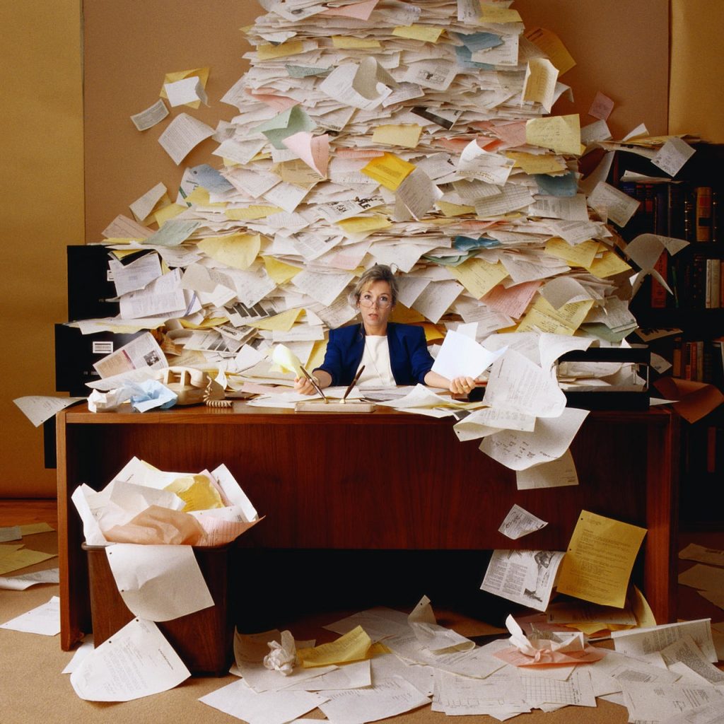 woman at desk with mountain of paperwork behind her